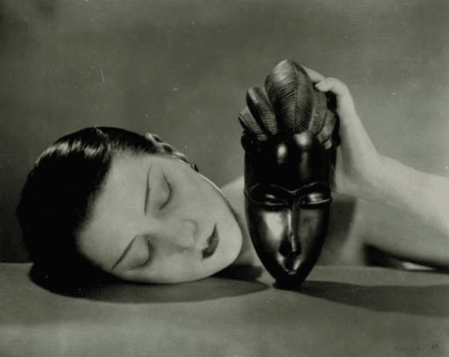 Man-Rays-most-famous-images-Noir-et-Blanche—a-Brancusi-like-face-of-a-woman-rests-on-a-table-while-she-holds-up-a-dark-African-mask—first-appeared-in-Paris-Vogue-in-1926