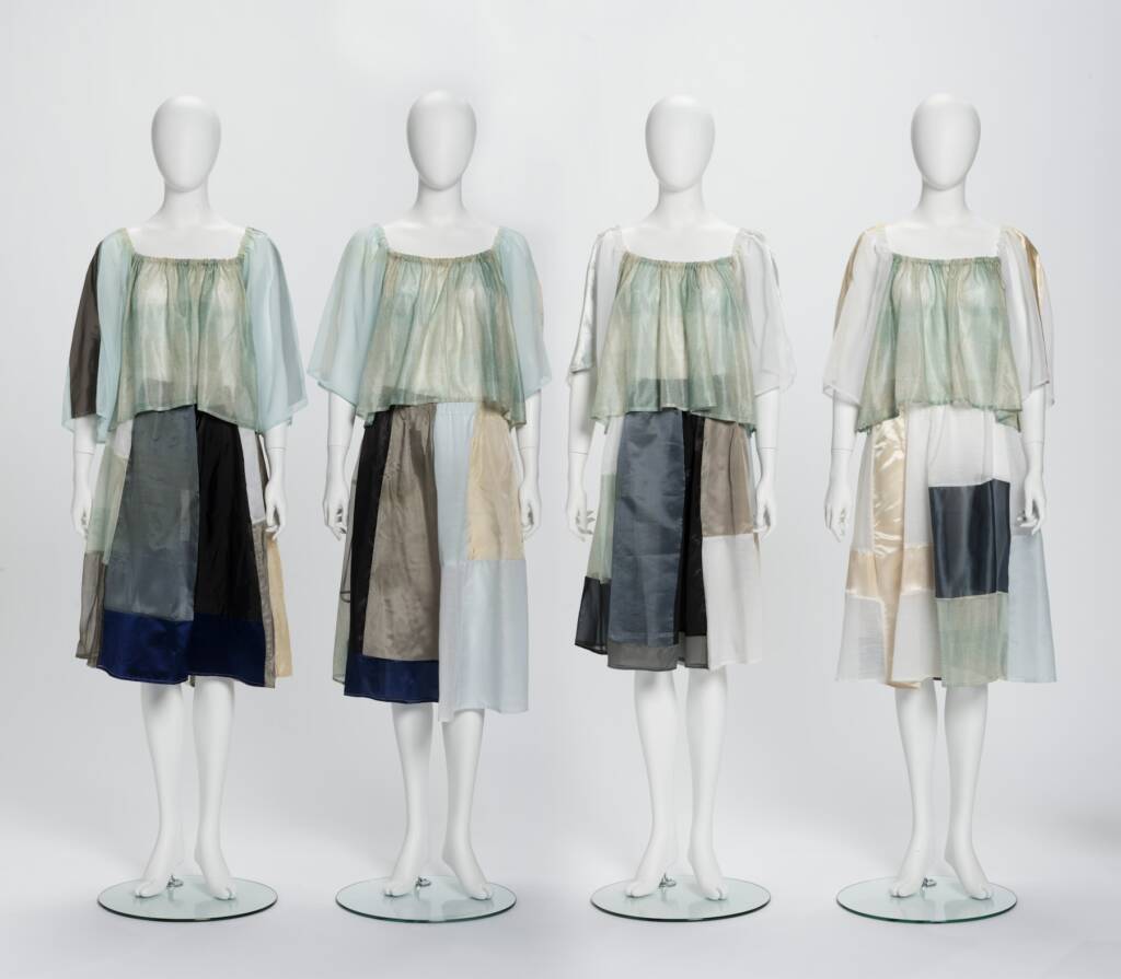 four mannequins in translucent skirt and top sets. the sets are made with a patchwork of cool-toned panels in shades of grey, blue, and green.